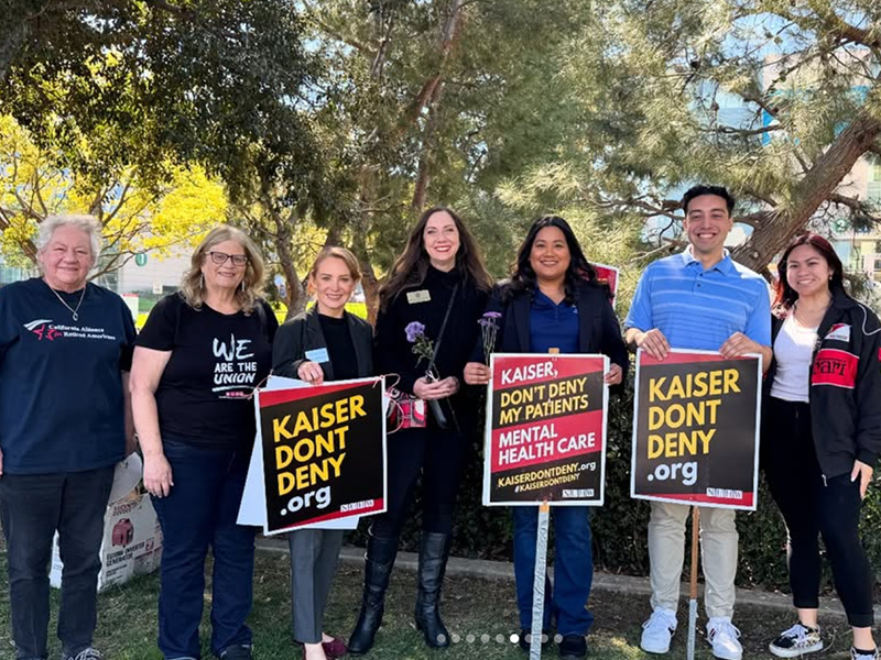Councilmember Jessie Lopez standing with Kaiser Permanente demonstrators holding protest signs.