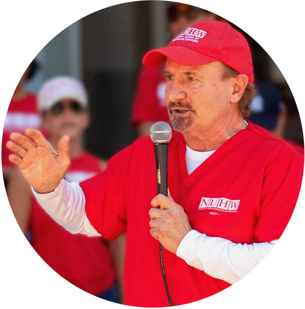 NUHW President Emeritus, Sal Roselli, holding a microphone while speaking to a crowd.