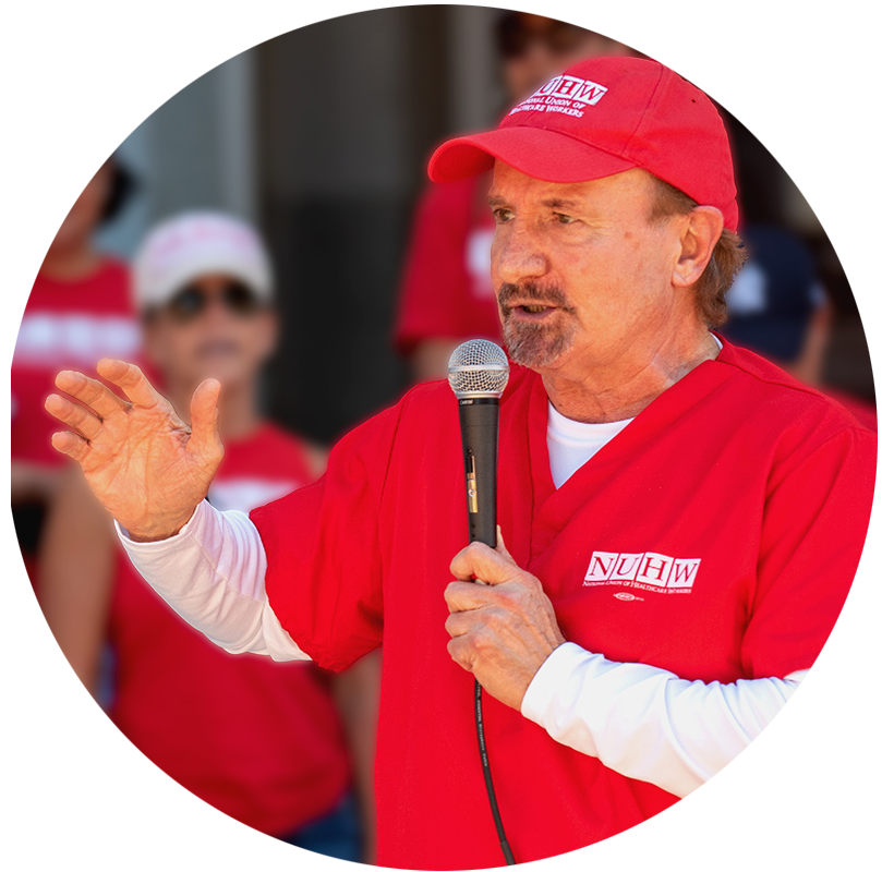 NUHW President Emeritus, Sal Rosselli, dressed in red and addressing a crowd holding a microphone.