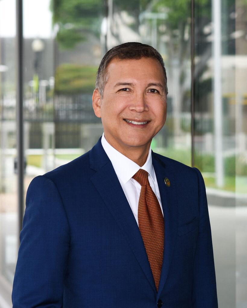 A portrait of OC Supervisor Vicente Sarmiento, smiling and wearing a blue suit with a red tie.