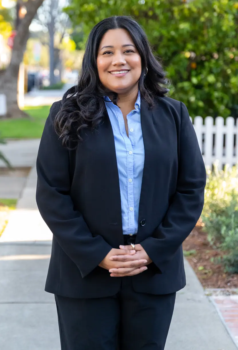 Jessie Lopez smiling with her hands folded in front of a residential neighborhood.