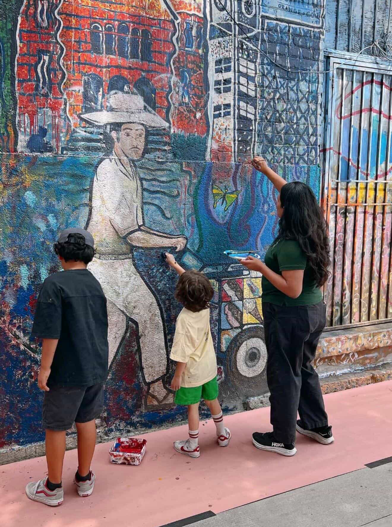 Jessie Lopez restoring a colorful mural with two children in Santa Ana.