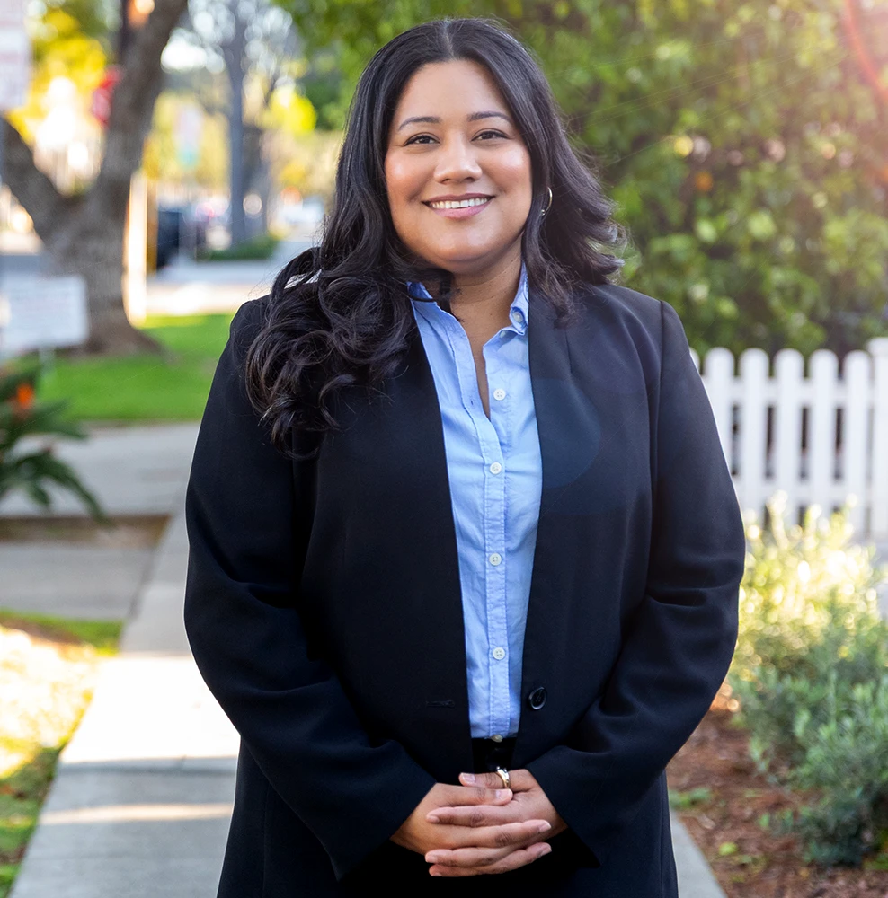 Jessie Lopez, smiling with hands folded, in front of a residential street.
