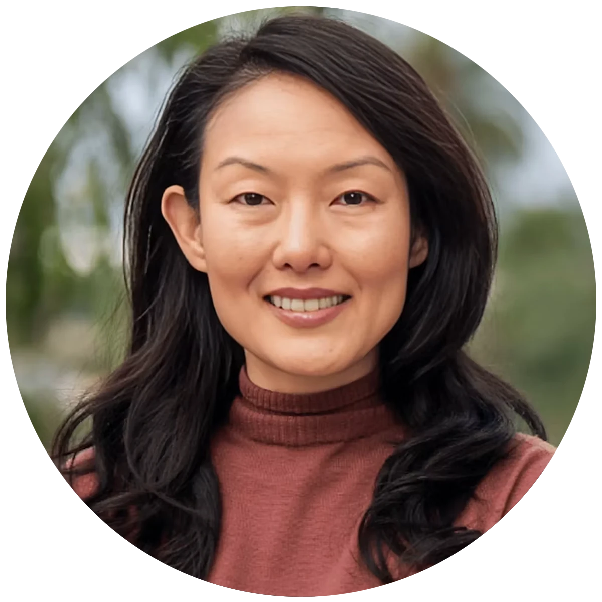 California Insurance Commissioner candidate, Jane Kim, smiling in front of a blurred tree background.