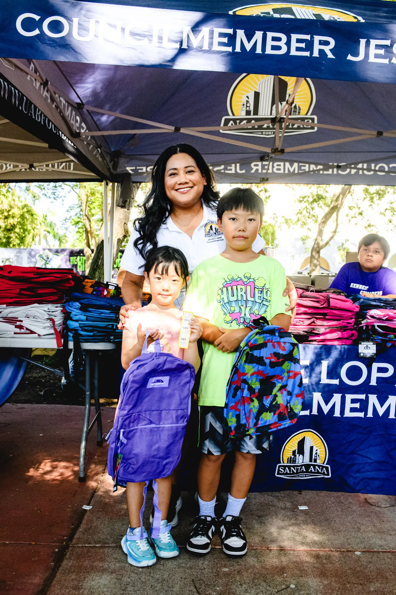 Jessie Lopez smiling with two children showing off their new backpacks.
