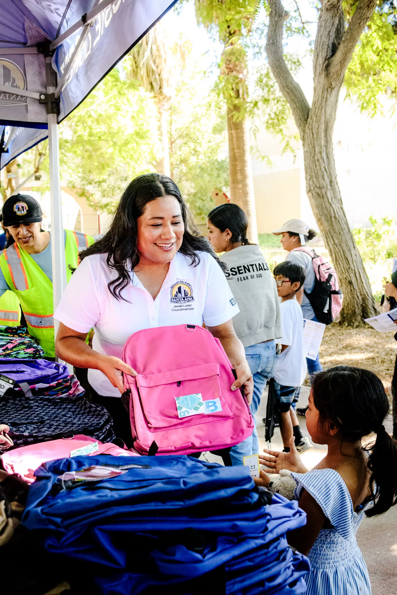 Jessie Lopez, smiling, handing a pink backpack to a little girl.