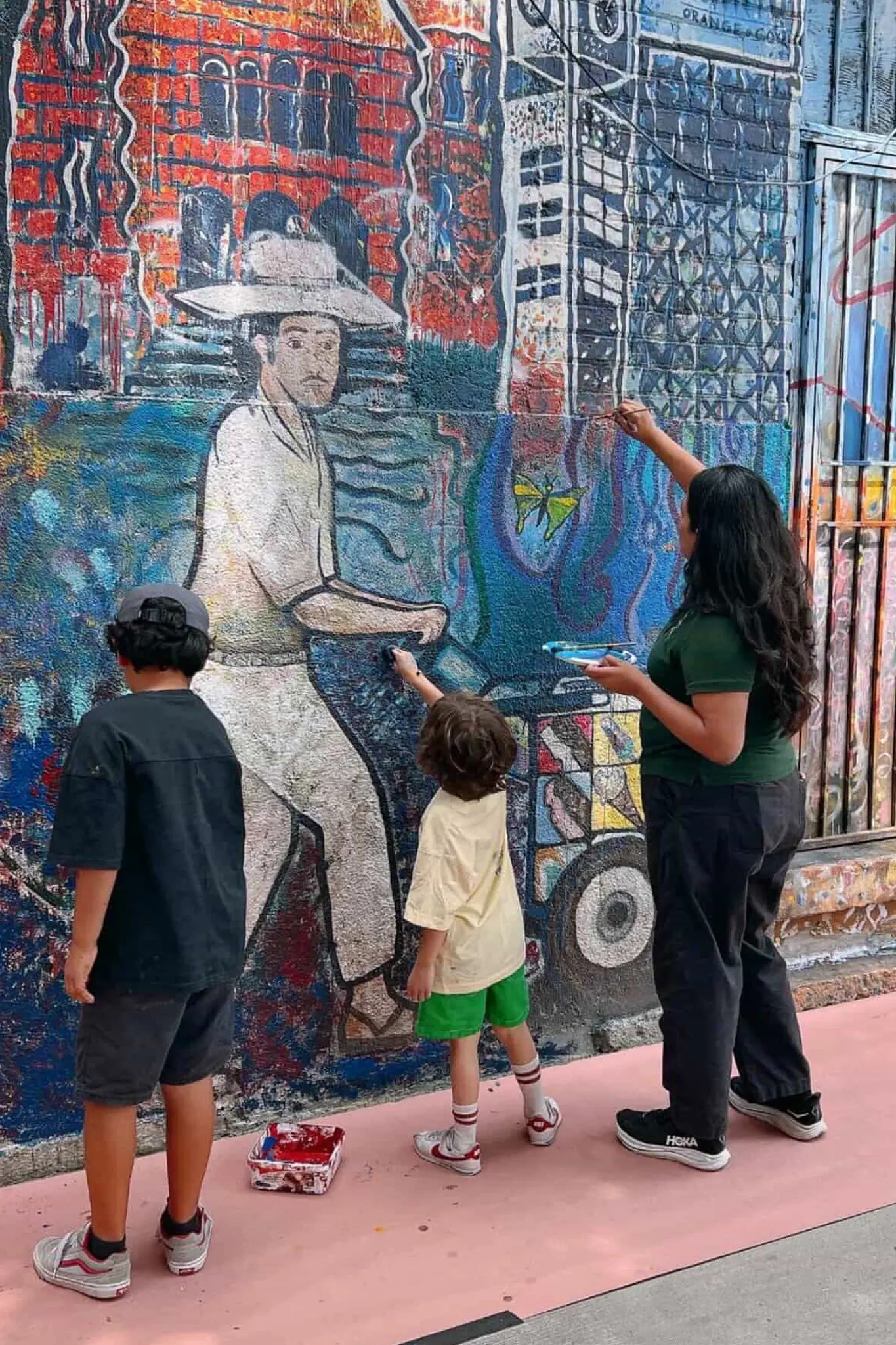 Jessie Lopez restoring a mural with two children in Santa Ana.